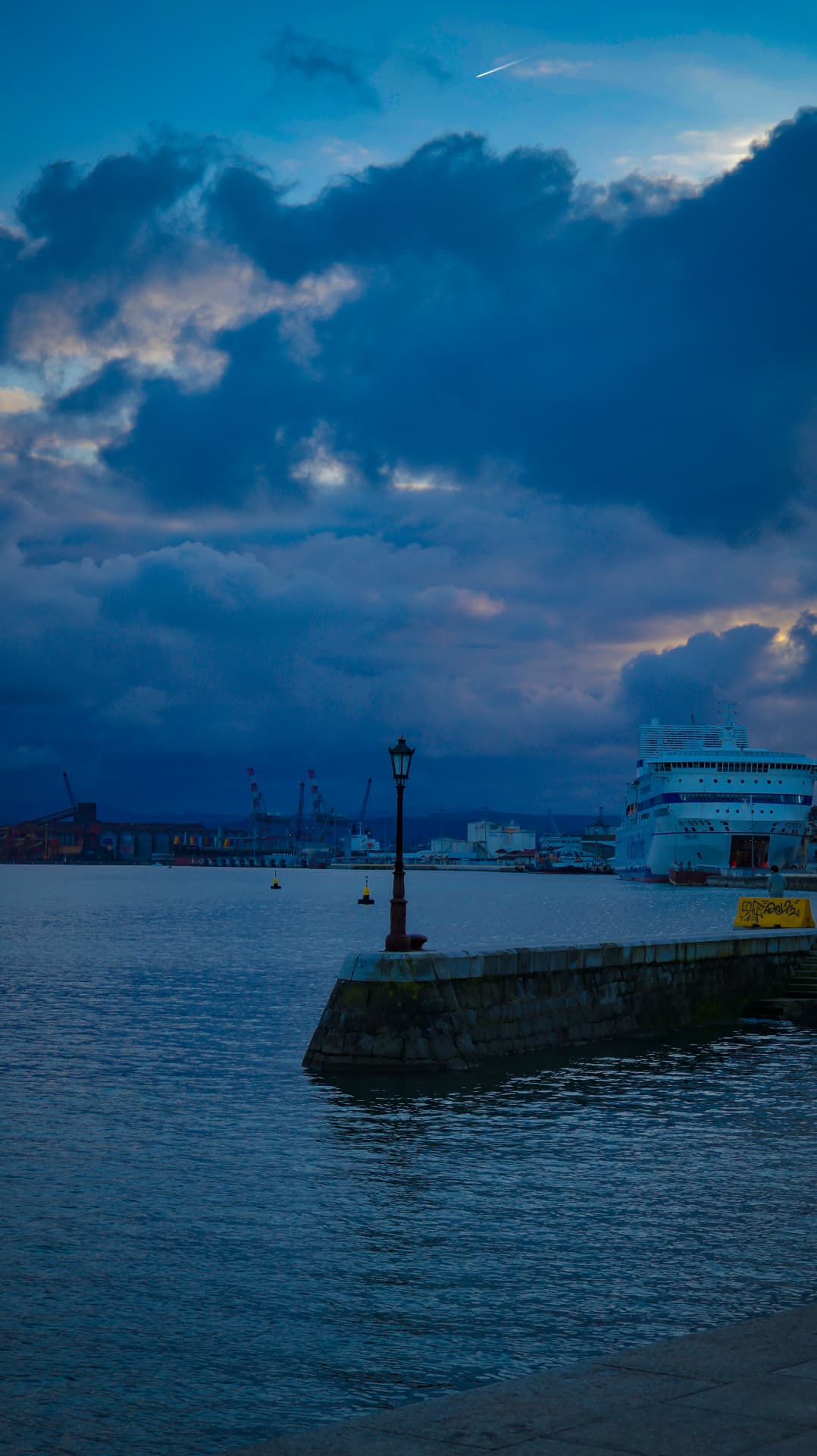 Puerto al anochecer con faro y crucero bajo nubes azules