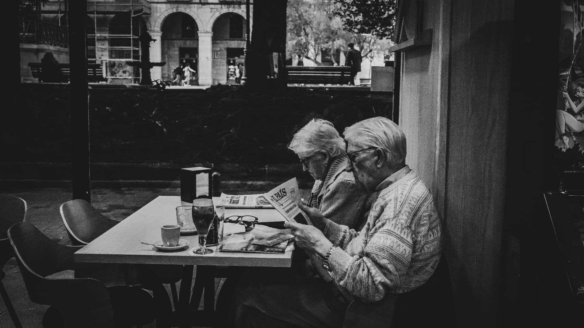 Dos señores leyendo el periódico en una terraza de café, blanco y negro